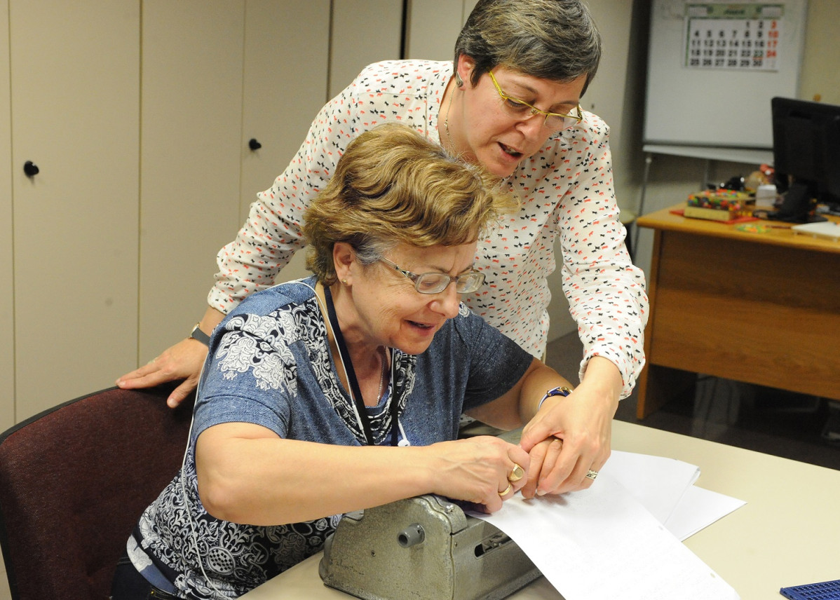 Una profesora de braille enseu00f1a a una mujer con discapacidad visual el manejo de una mu00e1quina Perkins