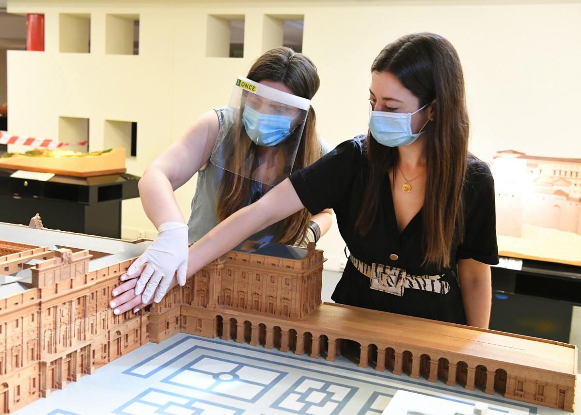 Una persona con discapacidad visual toca una maqueta, junto a una guu00eda del museo, ataviada con mascarilla, mu00e1scara y guantes  1499