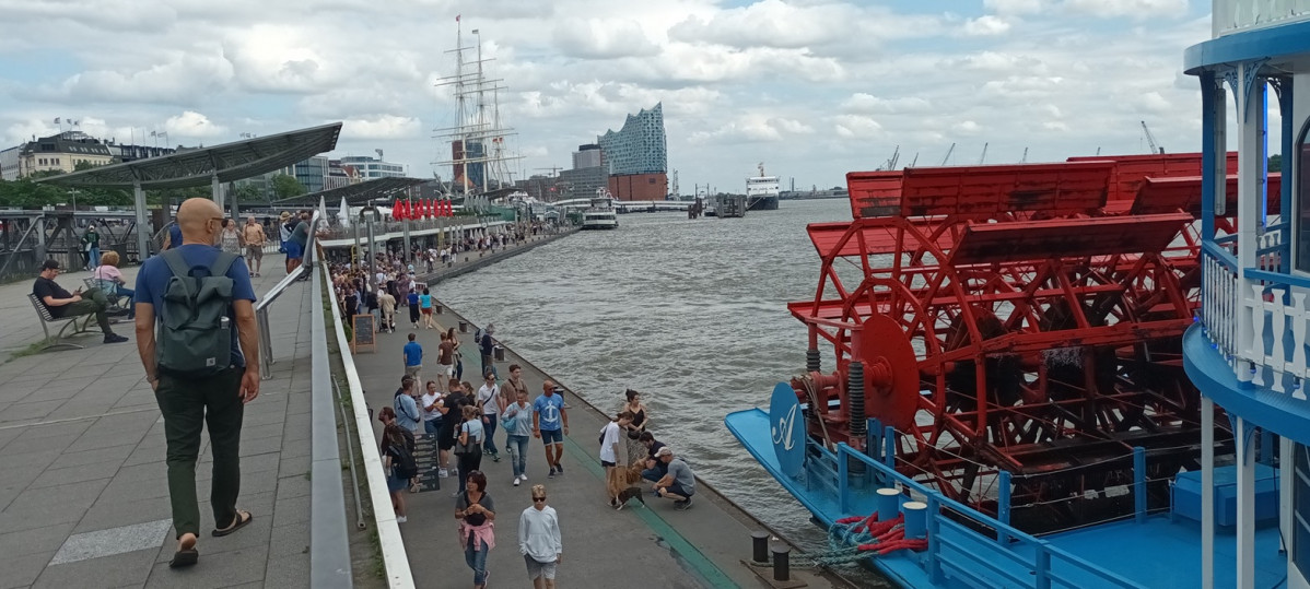 Turistas paseando por los muelles del puerto, al fondo el edificio de la Elbphylharmonie.